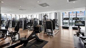 Una palestra moderna con diverse macchine per esercizi, ampie finestre e vista sullo skyline della città.
