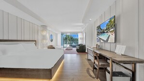 Una moderna camera d'albergo con un letto grande, una scrivania con una sedia, una TV e vista su una piscina e palme.