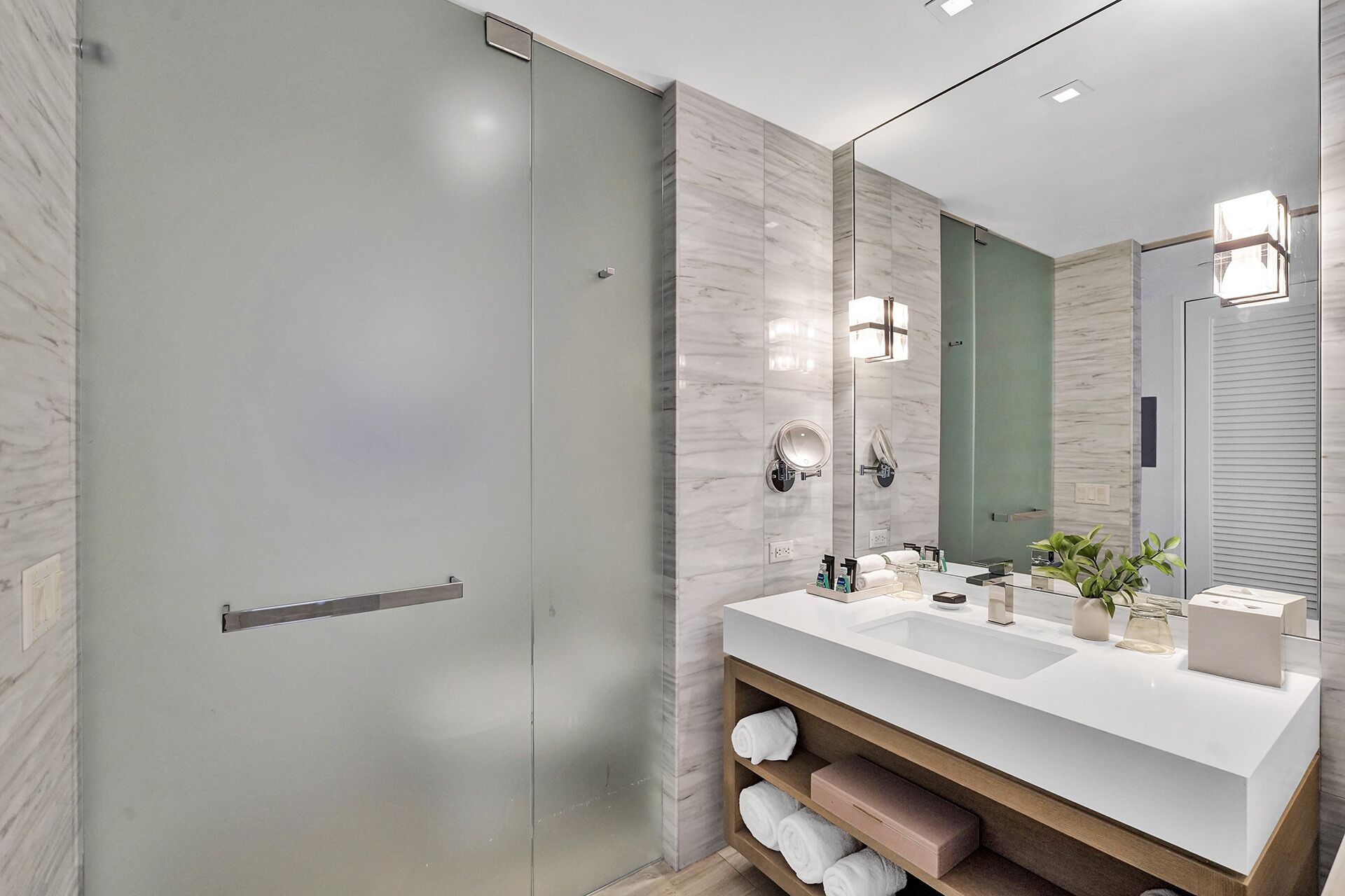 A modern bathroom with a glass shower door, a white sink with a mirror, and a wooden vanity.