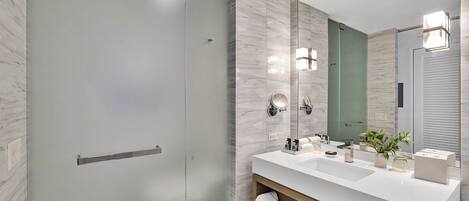 A modern bathroom with a glass shower door, a white sink with a mirror, and a wooden vanity.