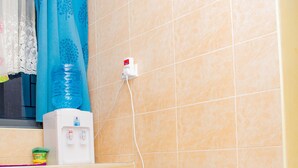 Una cocina compacta con refrigerador, dispensador de agua y cortina de ducha azul.