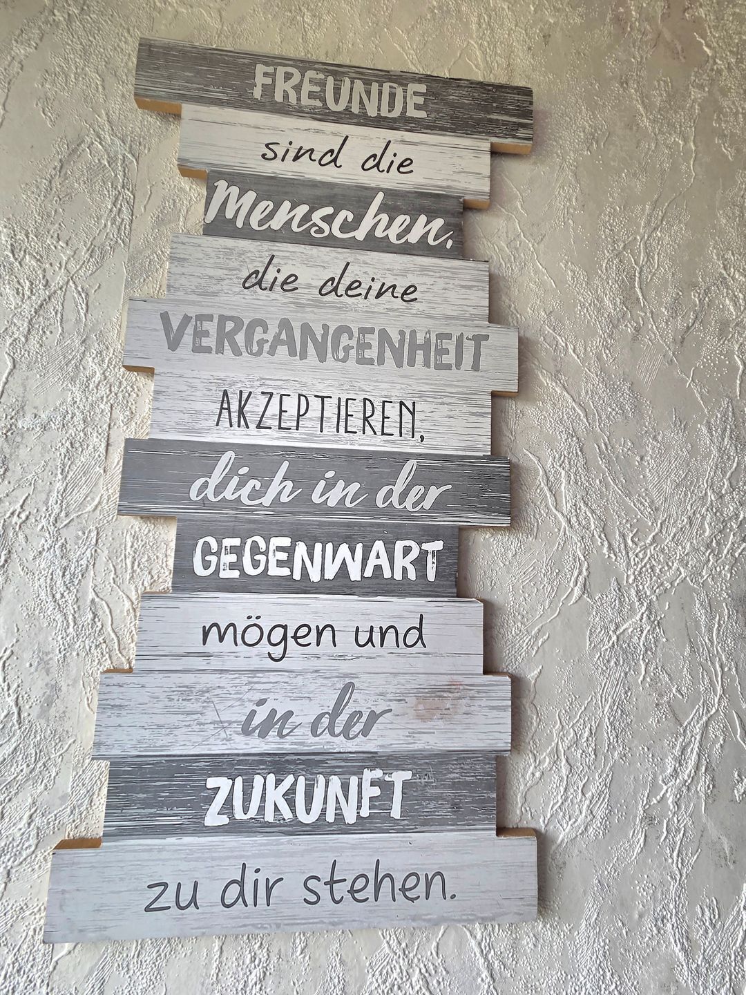 Une série de panneaux en bois portant des inscriptions en allemand, disposés verticalement contre un mur à texture.