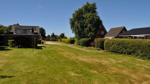A residential area with a well-maintained lawn, a large tree, and houses with visible driveways. - Haus Dorfschmiede, Whg. Seestern - Haus Dorfschmiede (Alkersum)