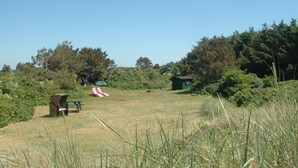 A grassy field with a picnic table, a small shed, and a red and white slide. - Haus Dorfschmiede, Whg. Seestern - Haus Dorfschmiede (Alkersum)