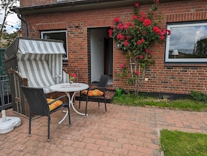 Una casa de ladrillo con un patio que tiene un toldo a rayas, mobiliario exterior y una enredadera de rosas.