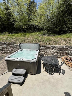 Un bain à remous avec un mur de pierres en arrière-plan, une table ronde en métal et deux chaises longues.