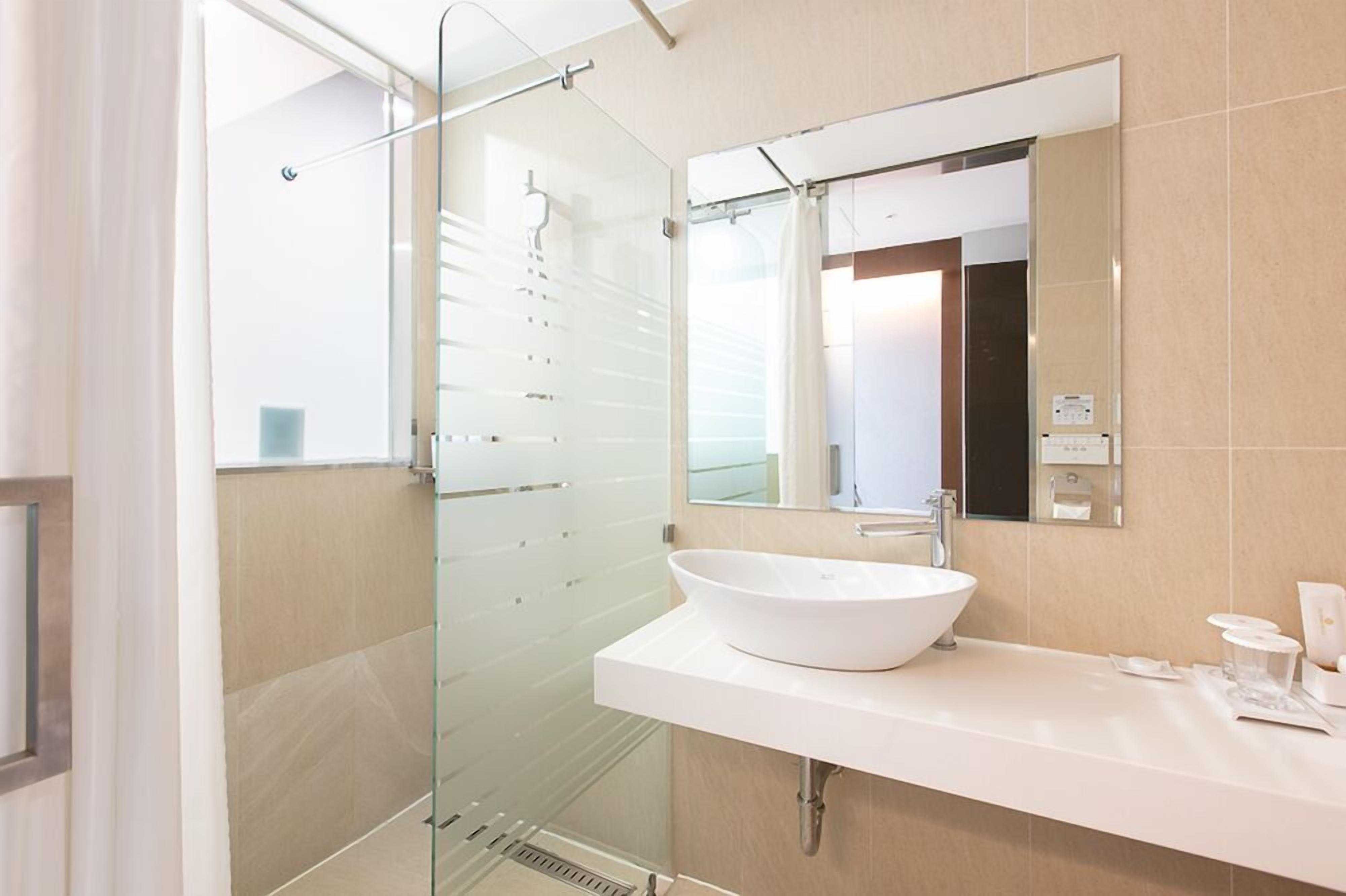 A modern bathroom with a glass shower enclosure, a white sink, and a large mirror.
