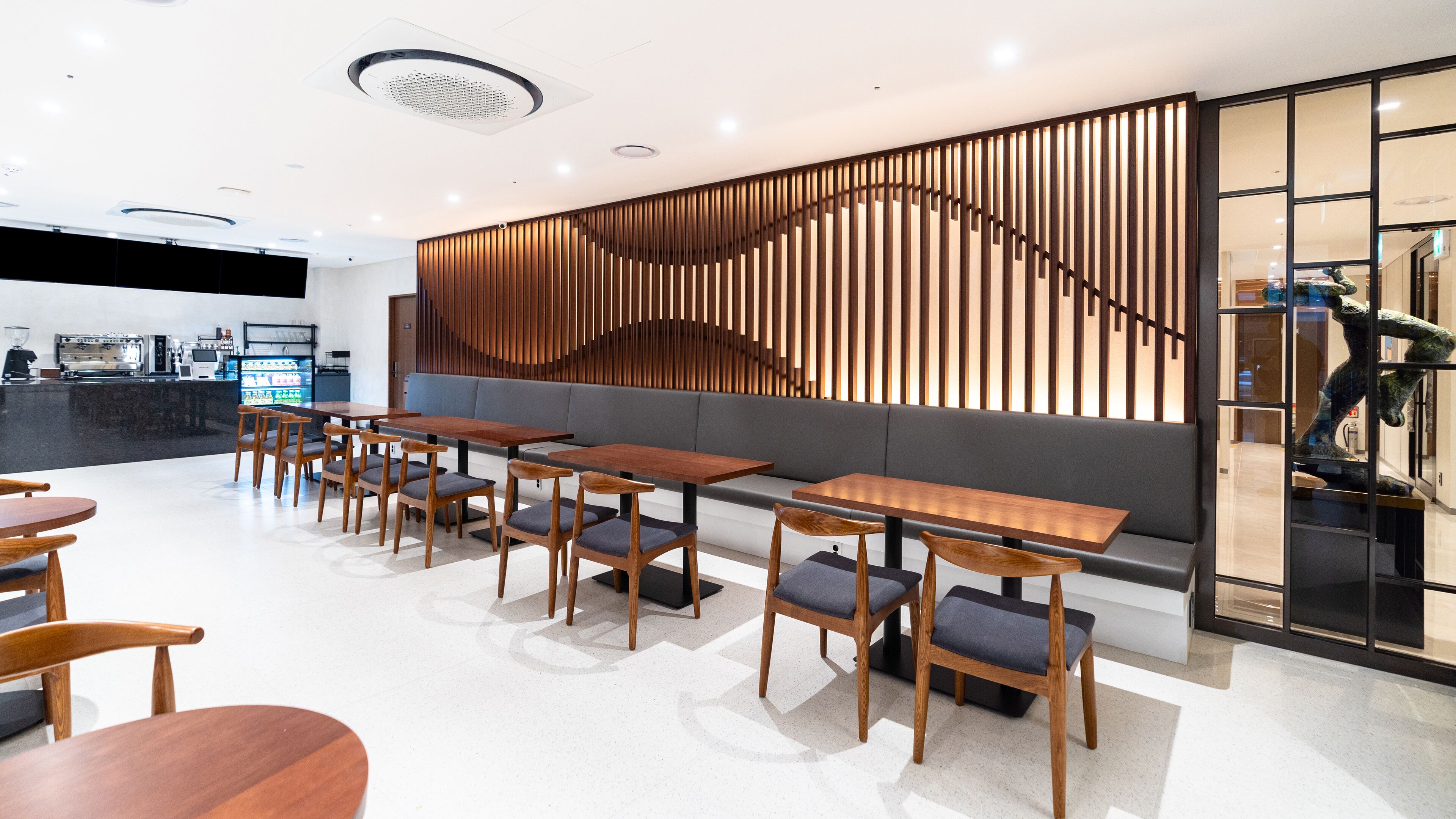 Een modern restaurant met houten tafels en stoelen, een bar met een koffieapparaat en een decoratief paneel aan de muur.