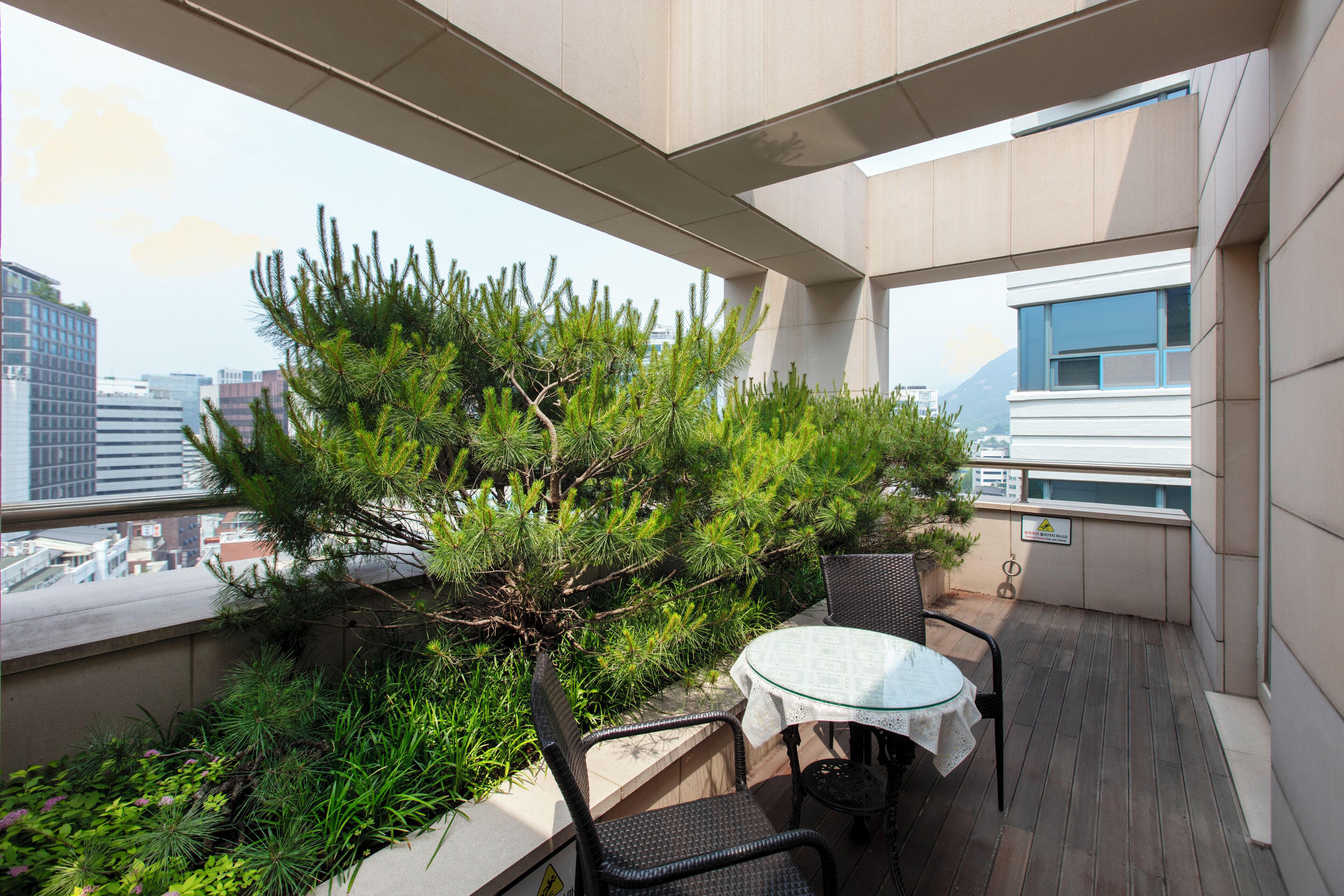 A balcony with a table and chairs, surrounded by greenery and overlooking a cityscape.