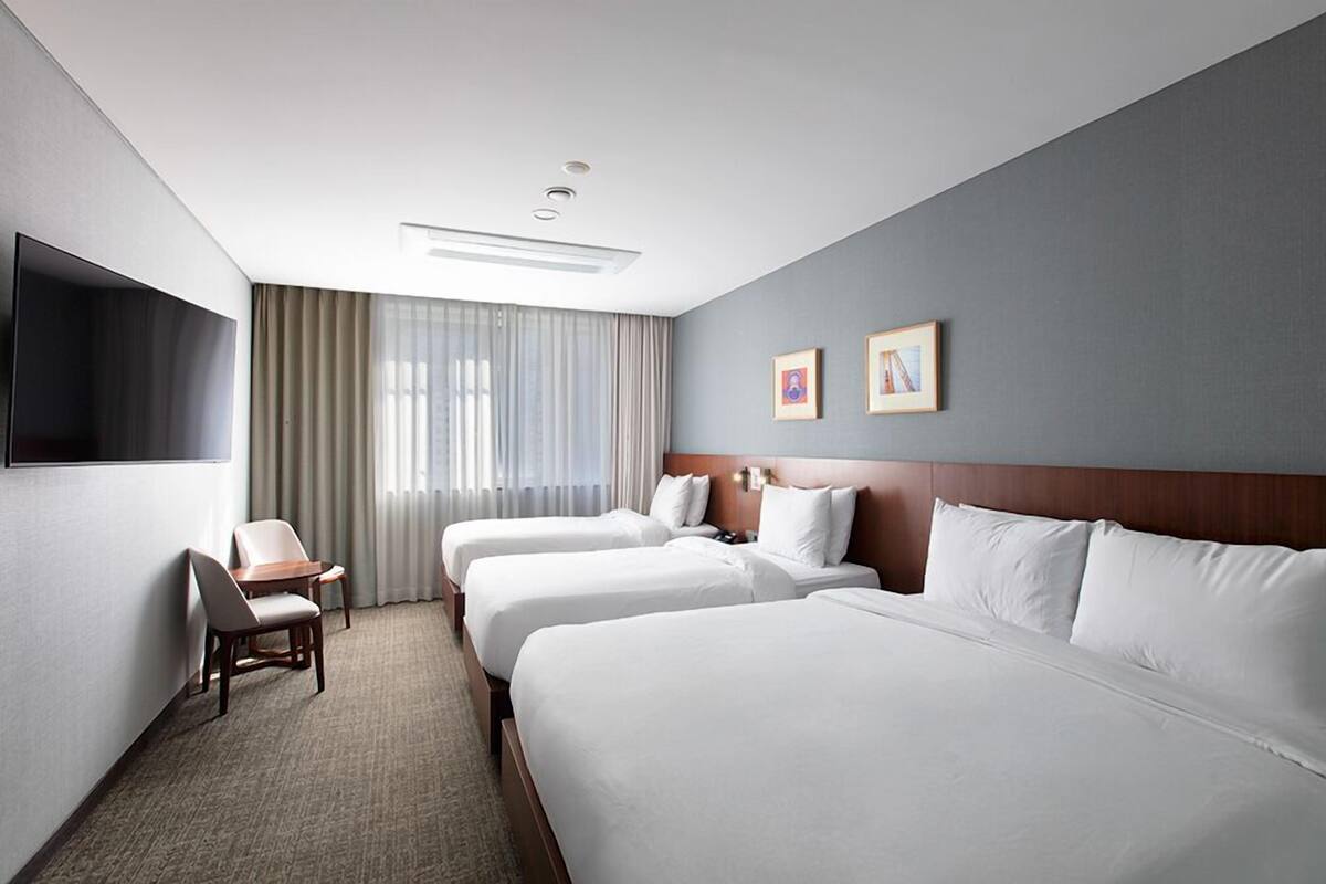 Une chambre d’hôtel avec trois lits, un bureau et une télévision.
