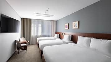 A hotel room with three beds, a desk, and a TV.