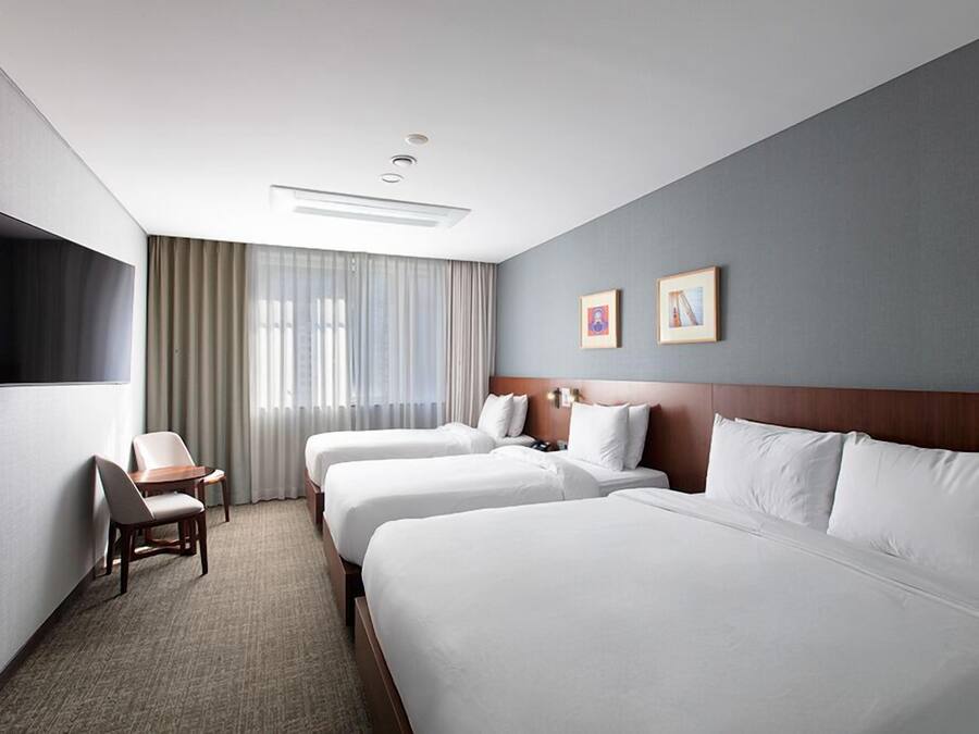A hotel room with three beds, a desk, and a TV.