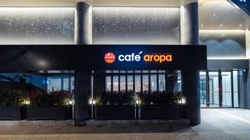 Un bâtiment moderne qui abrite un café appelé « Café Aropa », reconnaissable à son enseigne et à son entrée bien visibles.