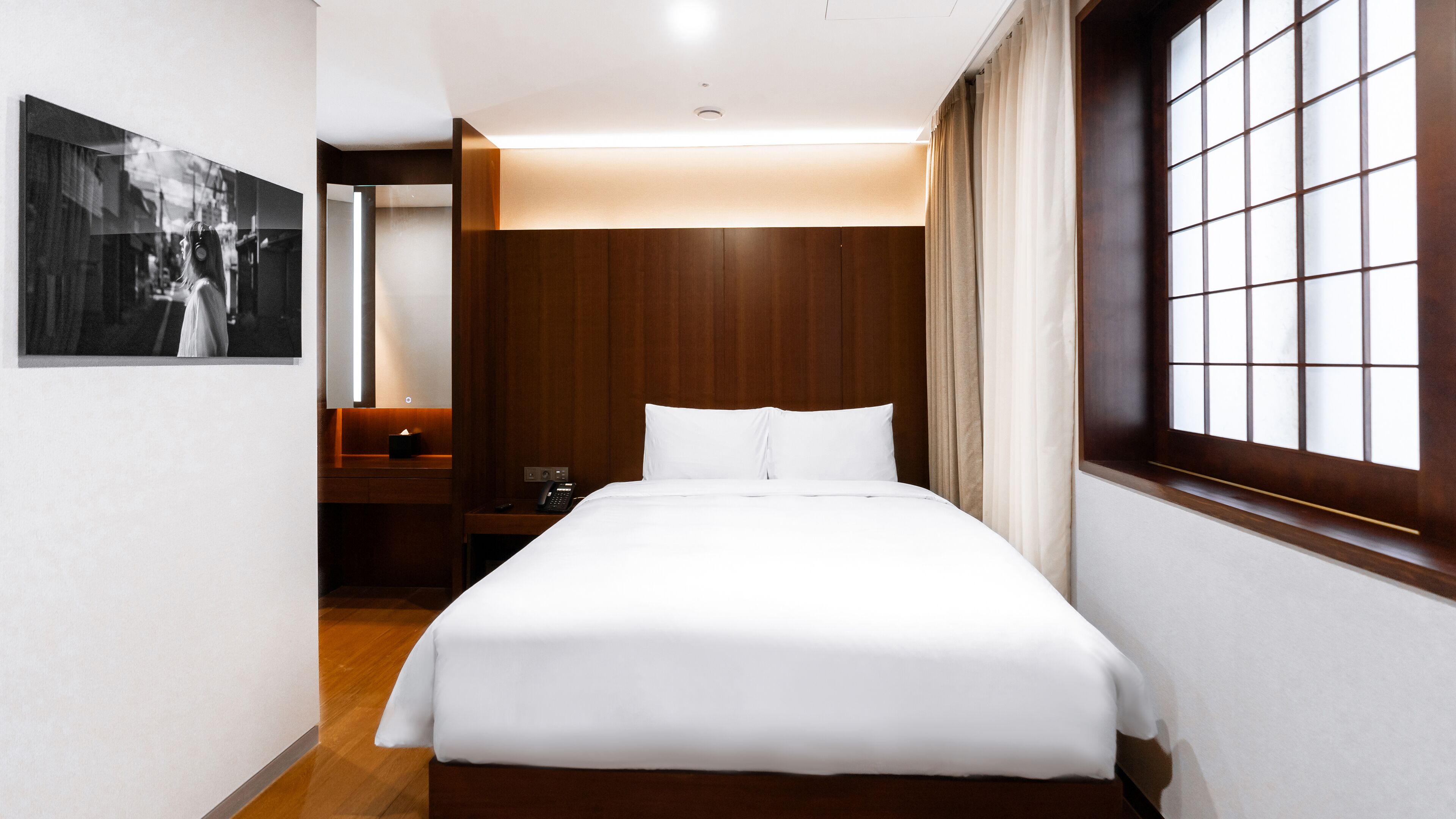 Una habitación de hotel con cama, mesita de noche y ventana con cortinas.