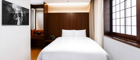 Una habitación de hotel con cama, mesita de noche y ventana con cortinas.