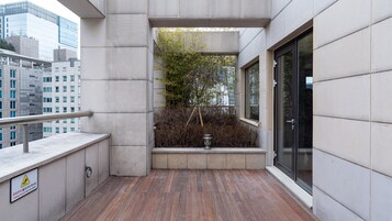 Un balcón con piso de madera, baranda de metal y vista a un paisaje urbano.