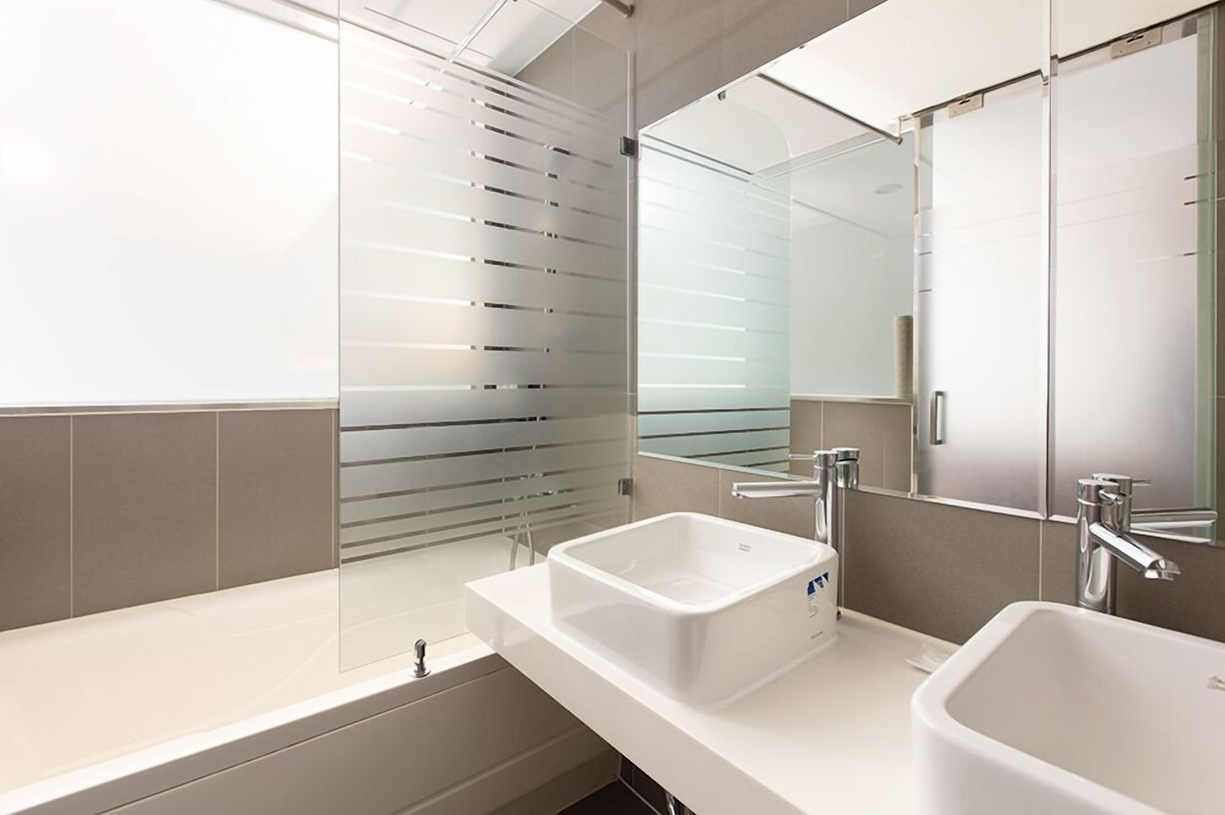 Un baño moderno con un espejo grande, dos lavamanos y una bañera.