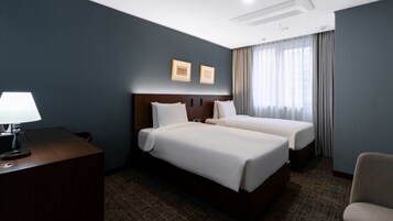 Habitación de hotel con dos camas, un escritorio con lámpara, una silla y una ventana con cortinas.