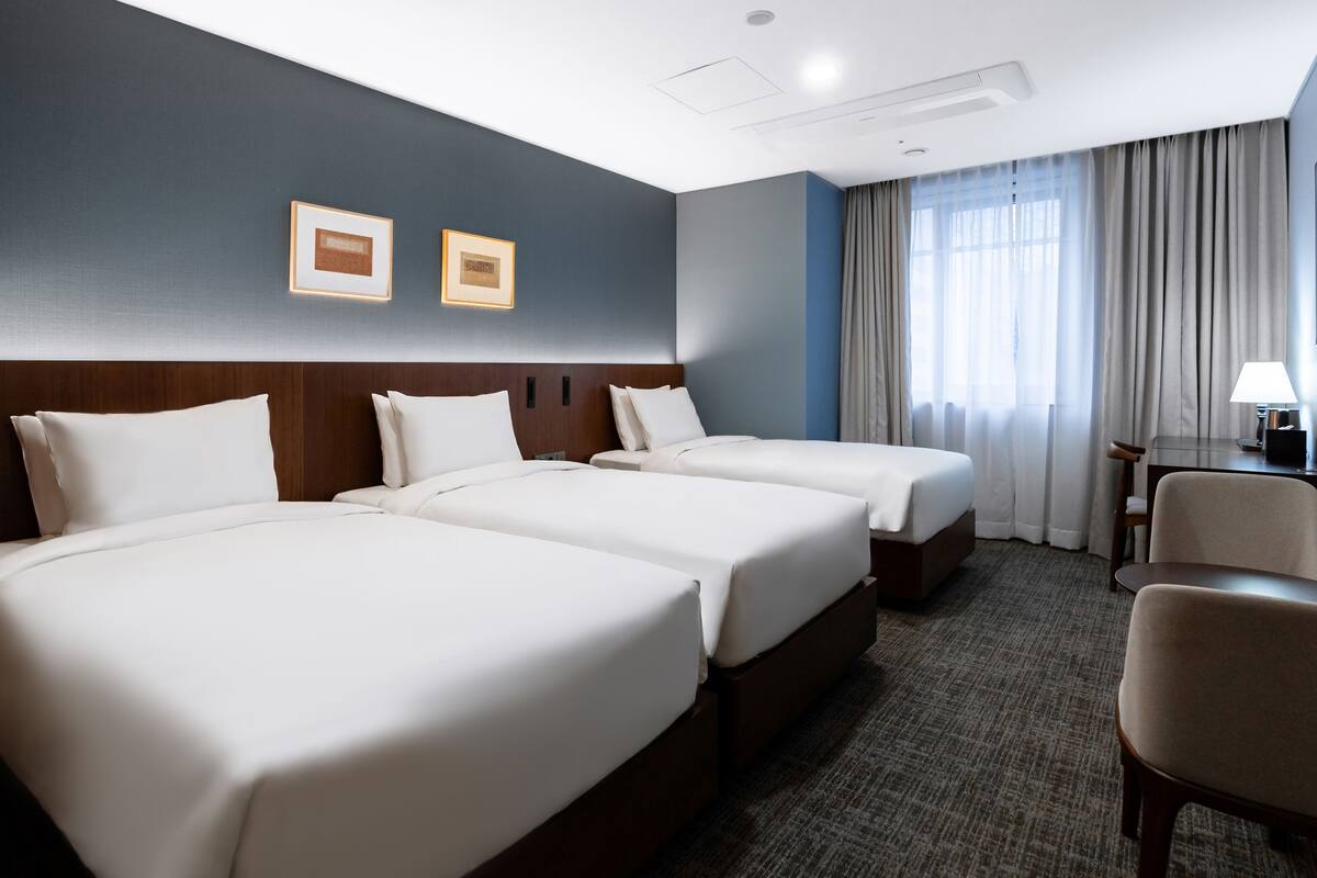 Une chambre d’hôtel avec deux lits, un bureau, une chaise et un téléviseur fixé au mur.