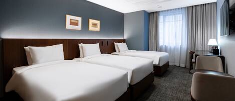 A hotel room with two beds, a desk, a chair, and a TV on the wall.