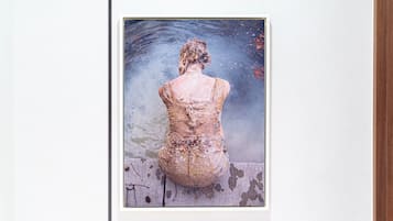 Una obra de arte enmarco que muestra una figura con vestido sentada junto al agua.