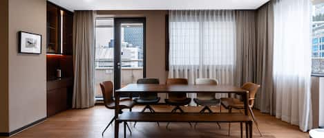 A modern conference room with a wooden table and chairs, large windows with curtains, and a city view.