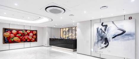 A modern lobby with a reception desk, a large painting of apples, and a black abstract painting.