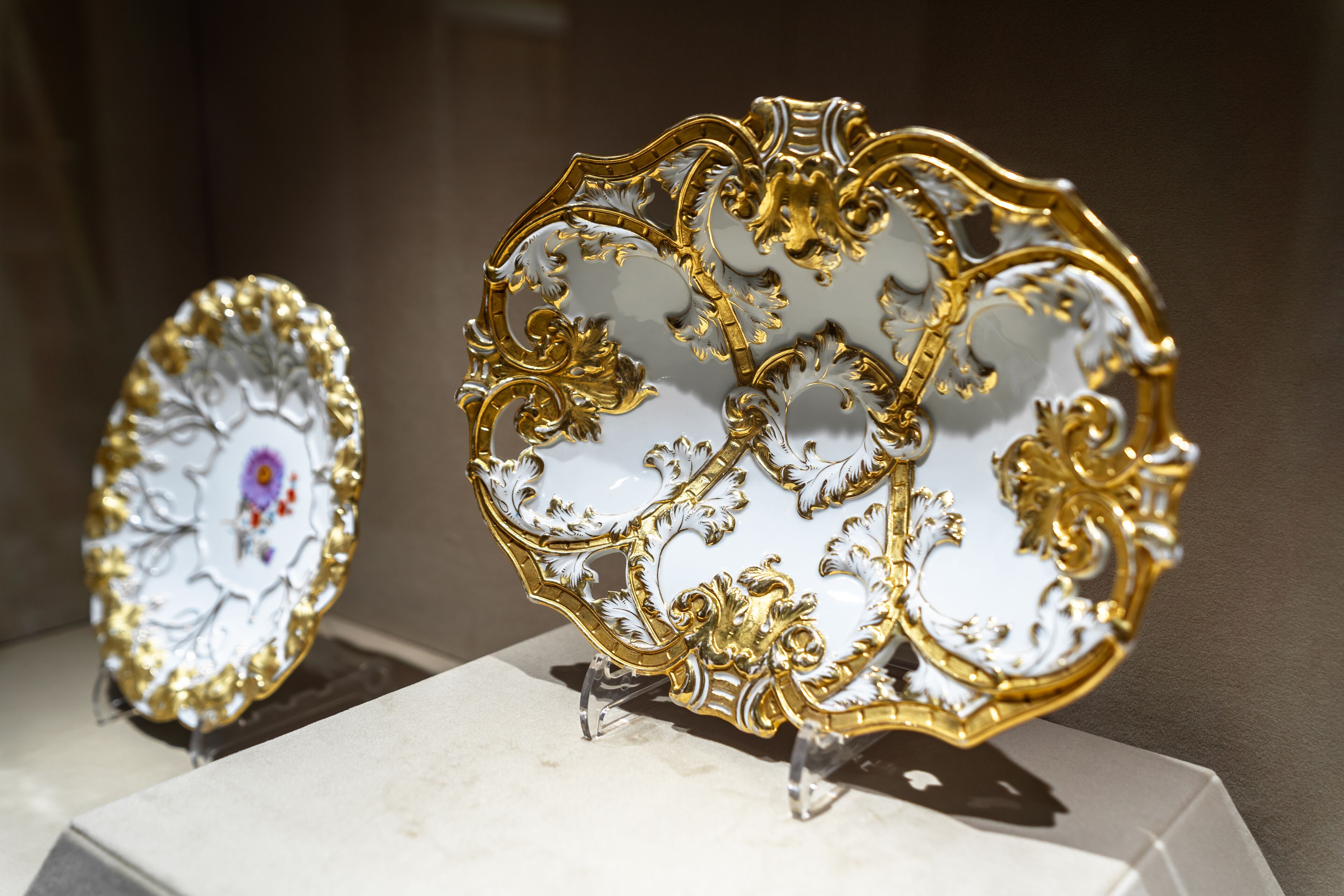 Dos platos de porcelana ornamentados con detalles dorados, exhibidos sobre soportes.