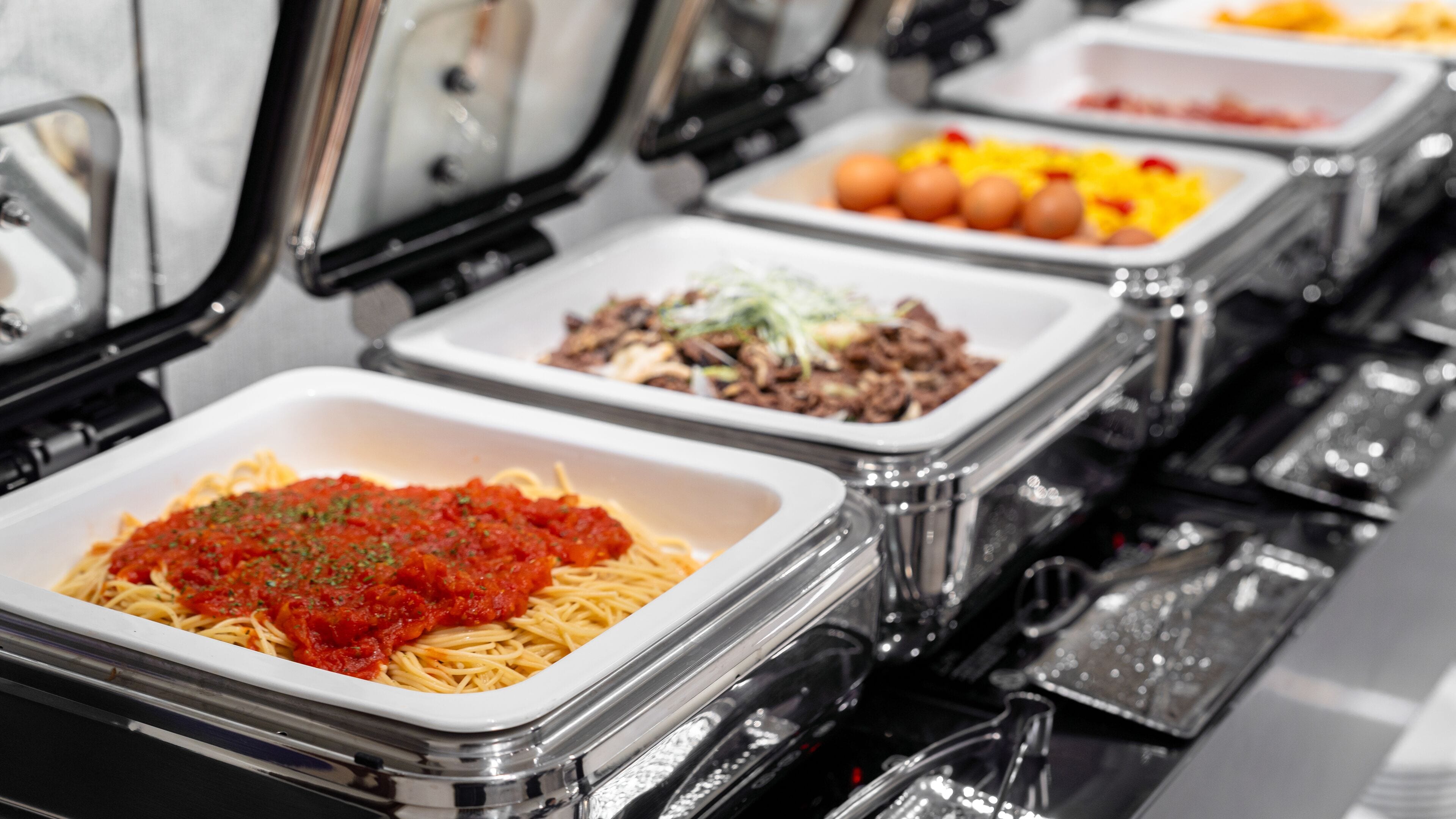 A buffet line with various dishes including pasta, meat, and vegetables.