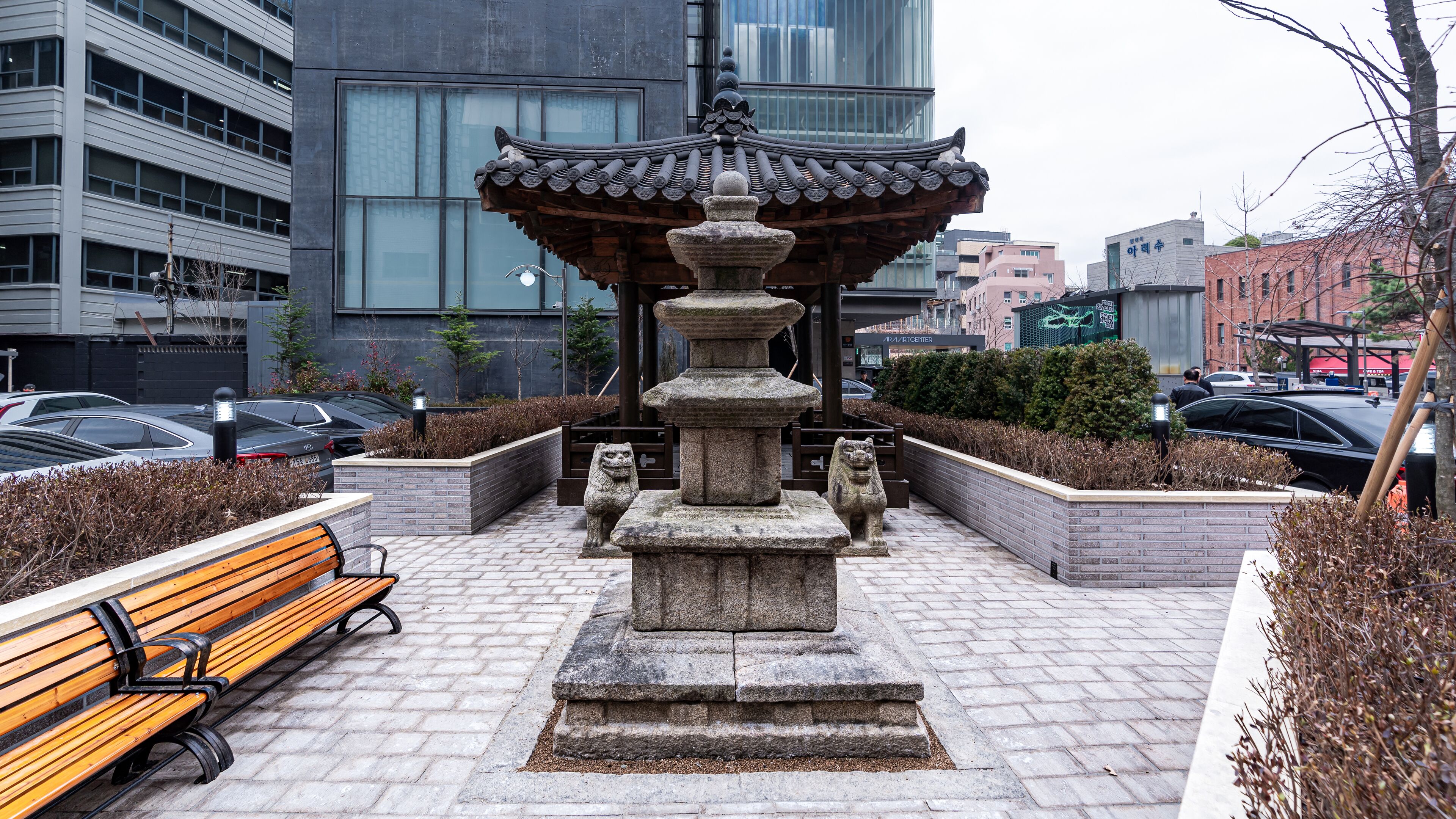 A stone fountain with a traditional roof, surrounded by a paved walkway and benches.