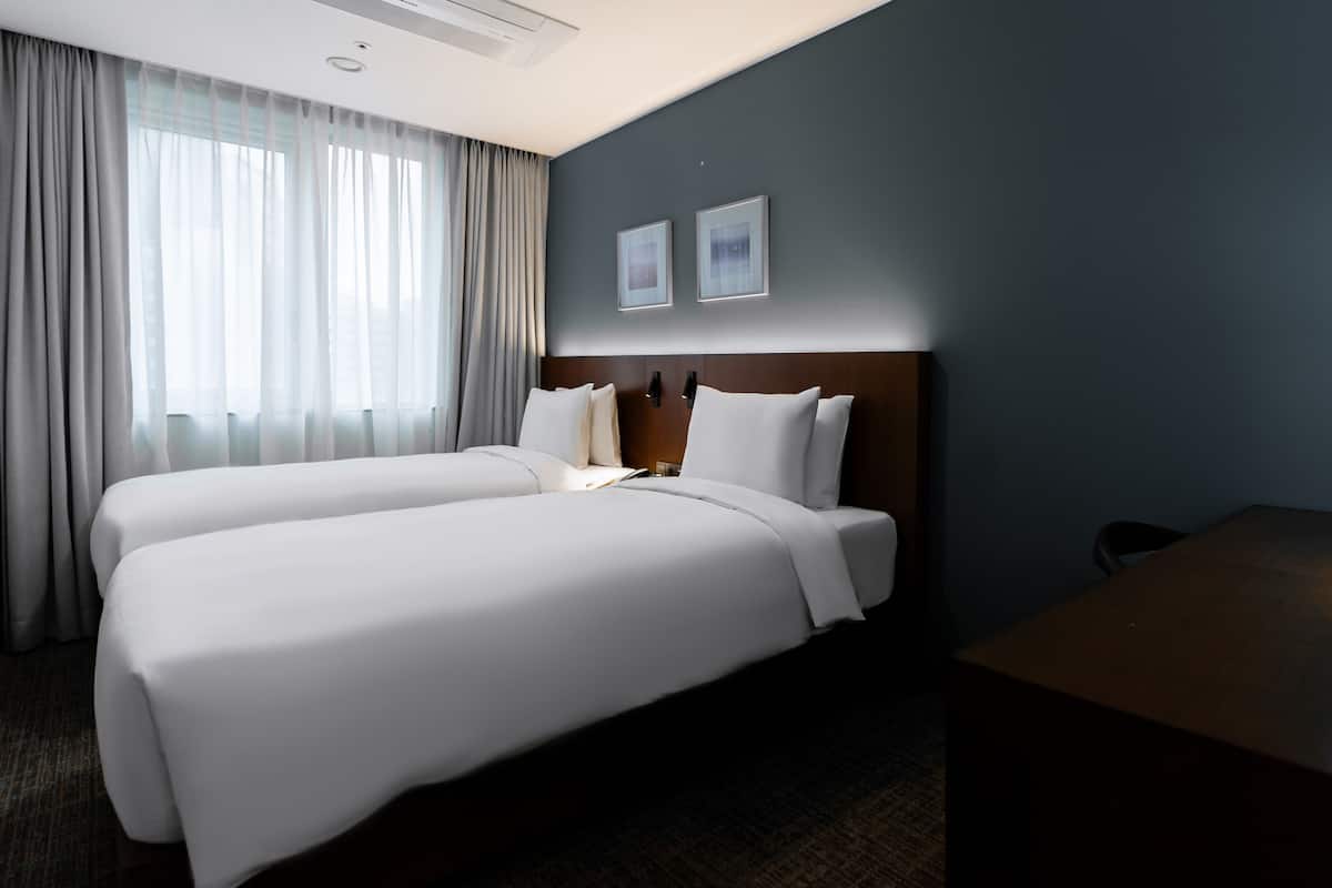 Une chambre d’hôtel avec deux lits, un bureau, une lampe et une fenêtre avec des rideaux.
