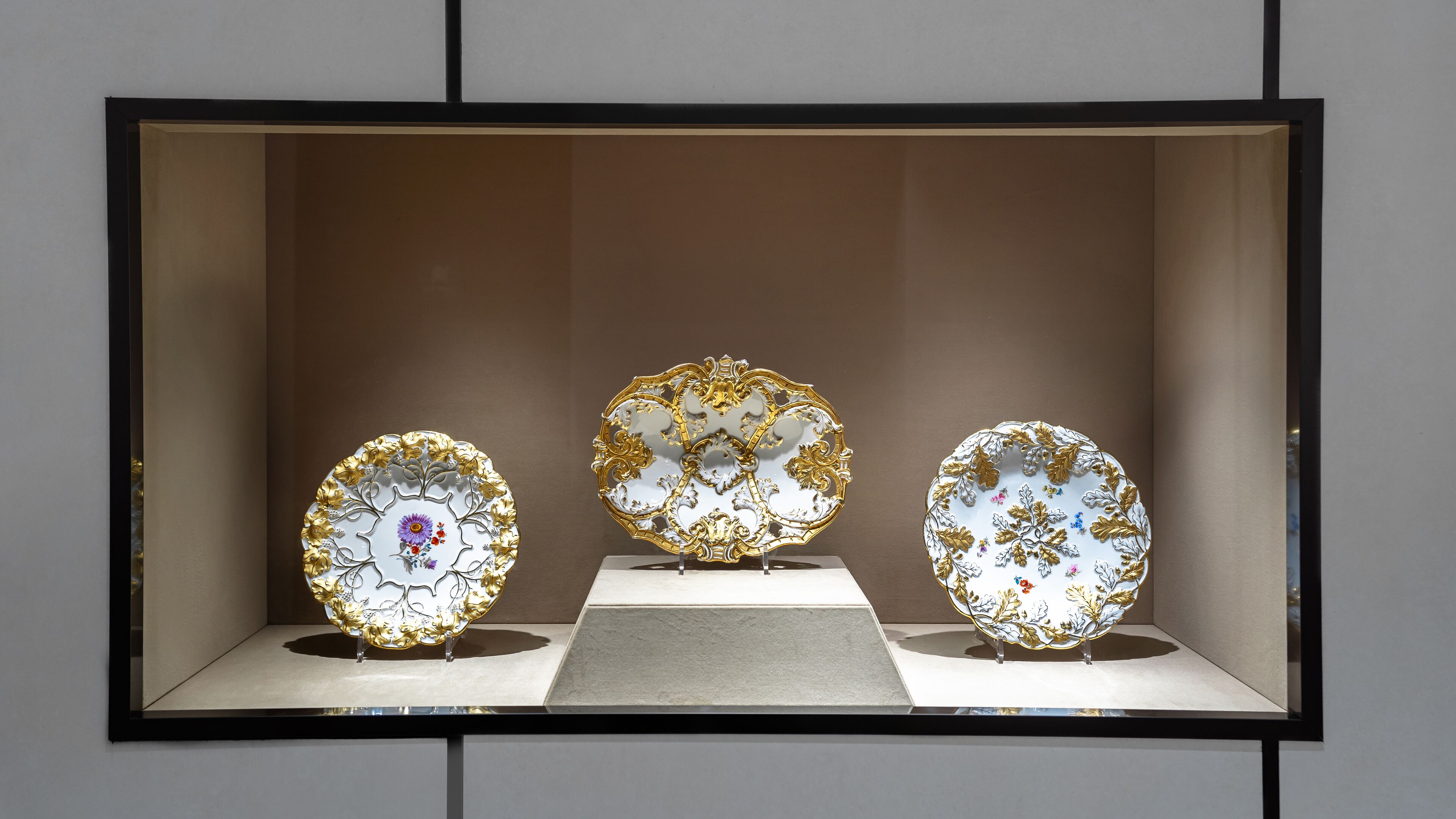 Three ornate plates displayed in a glass case.