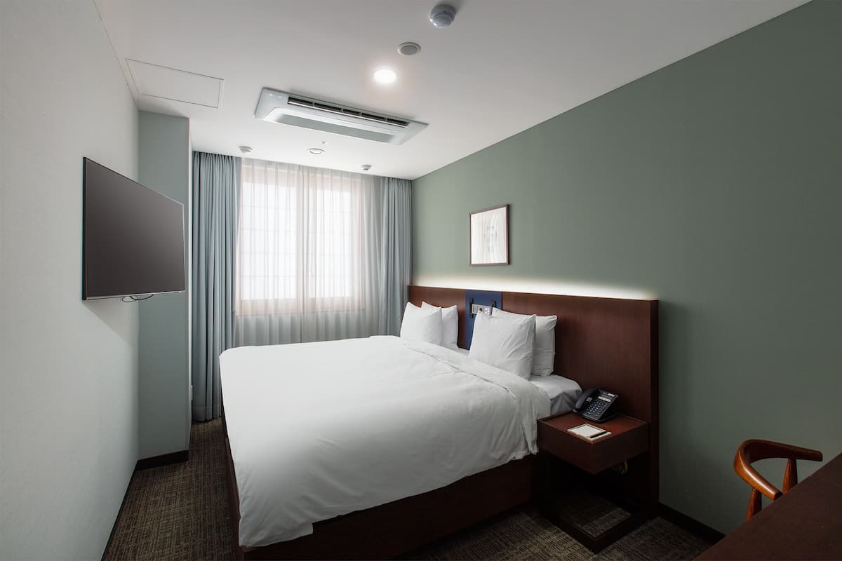 Une chambre d’hôtel équipée d’un lit, d’une table de chevet avec un téléphone et un bloc-notes, d’un téléviseur fixé au mur et d’un appareil de climatisation.