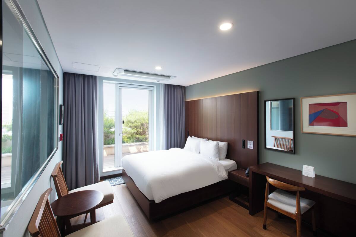 Une chambre d’hôtel moderne, dotée d’un grand lit, d’un bureau, d’une chaise et offrant une vue sur l’extérieur.