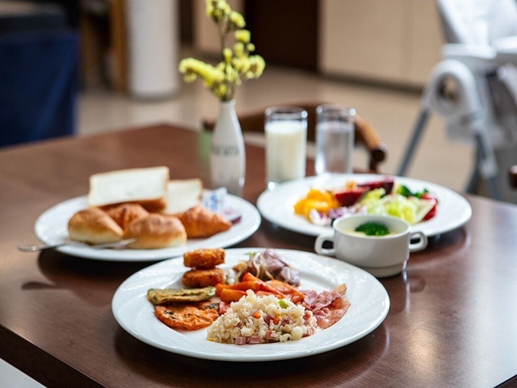 A breakfast table with plates of food, a vase with flowers, and a milk jug.
