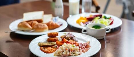 A breakfast table with plates of food, a vase with flowers, and a milk jug.