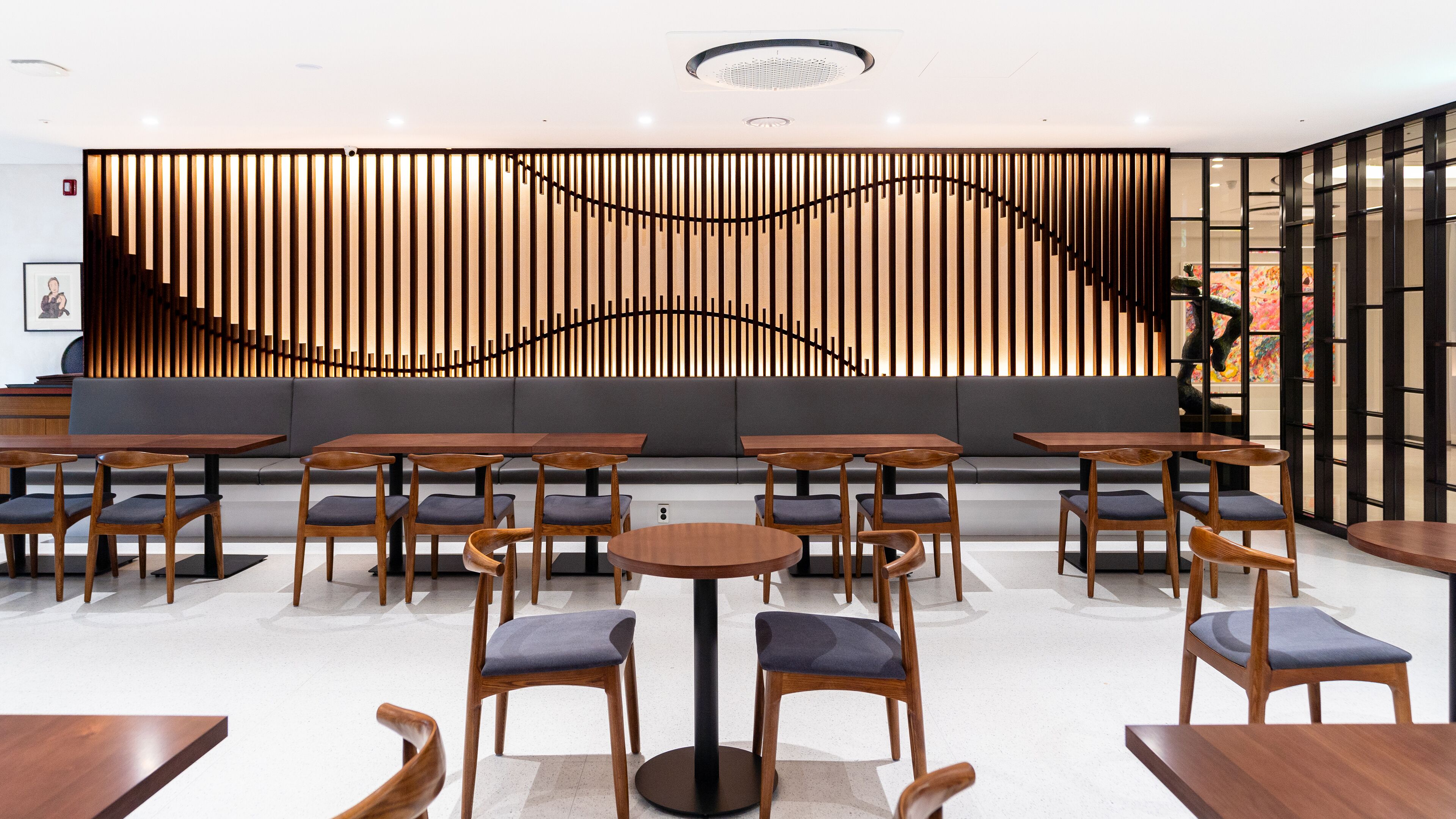 Een modern café met houten tafels en stoelen, een grijze bank en een decoratieve wand met verticale houten latten.