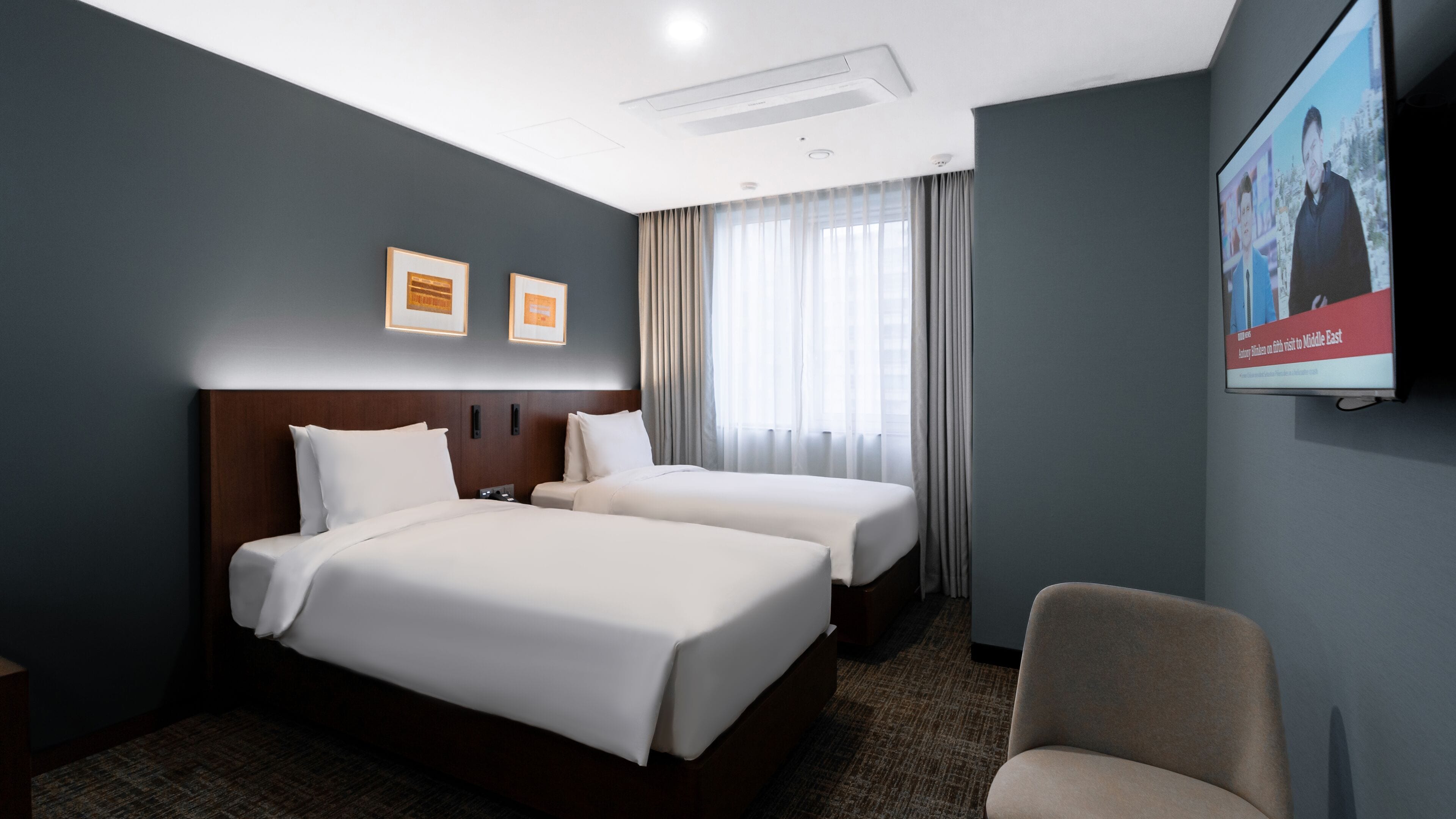 A hotel room with two beds, a TV, and a chair.