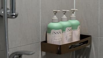 Ett badrum med grå kakelplattor och en hylla med tre flaskor av tvättlotionen INS Body Wash.