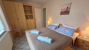 A bedroom with a bed, a chair, a wardrobe, a bedside table, and a lamp. - Haus Friesenglück, Whg. Silbermöve - Haus Friesenglück (Alkersum)
