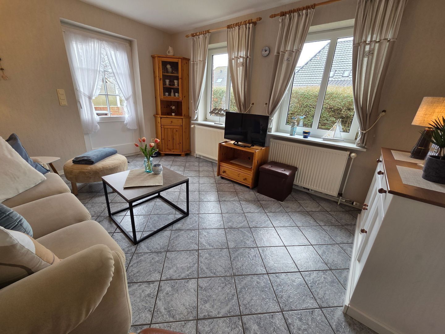 Een woonkamer met een bank, een salontafel, een tv-meubel, een kast en een raam met gordijnen.