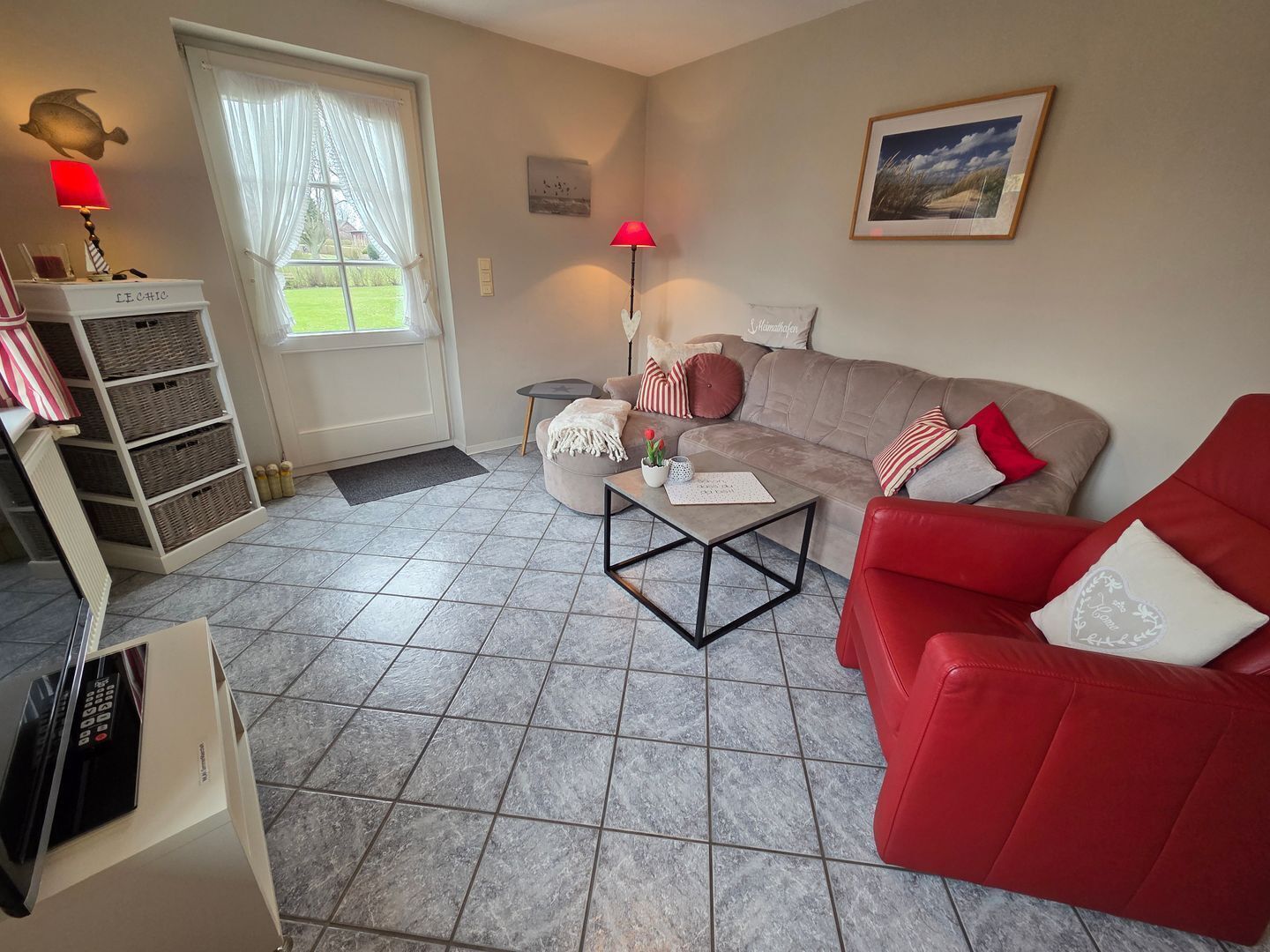 A living room with a sofa, a red chair, a coffee table, a lamp, a picture on the wall, and a window with curtains.