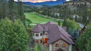 Una casa de piedra grande con torrecilla, rodeada de un bosque frondoso y un campo de golf.