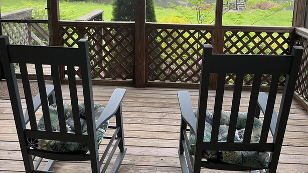 A covered porch with two rocking chairs, a wooden deck, and a view of a green landscape with trees and a gazebo. - Cozy cottage with a beautiful waterfront view. Pet friendly! 45 min from DC.   (Catharpin)