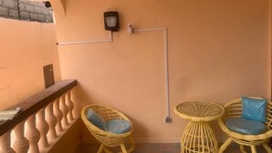 A balcony with a railing, two wicker chairs with cushions, a small round table, and a wall-mounted electrical outlet. - Sans thème (Cotonou)