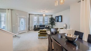 A modern living room with a sofa, a dining table with chairs, and a kitchen area with a bowl on the table.