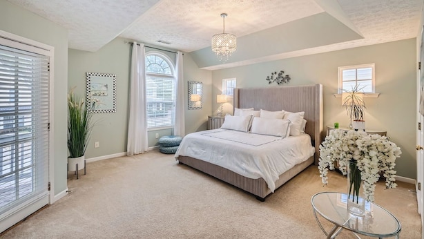 A bedroom with a large bed, a chandelier, and a vase of flowers.