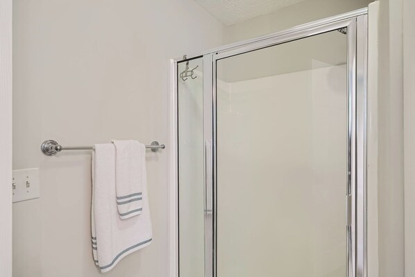 A bathroom with a glass shower door, a towel rack with a white towel, and a visible electrical outlet.