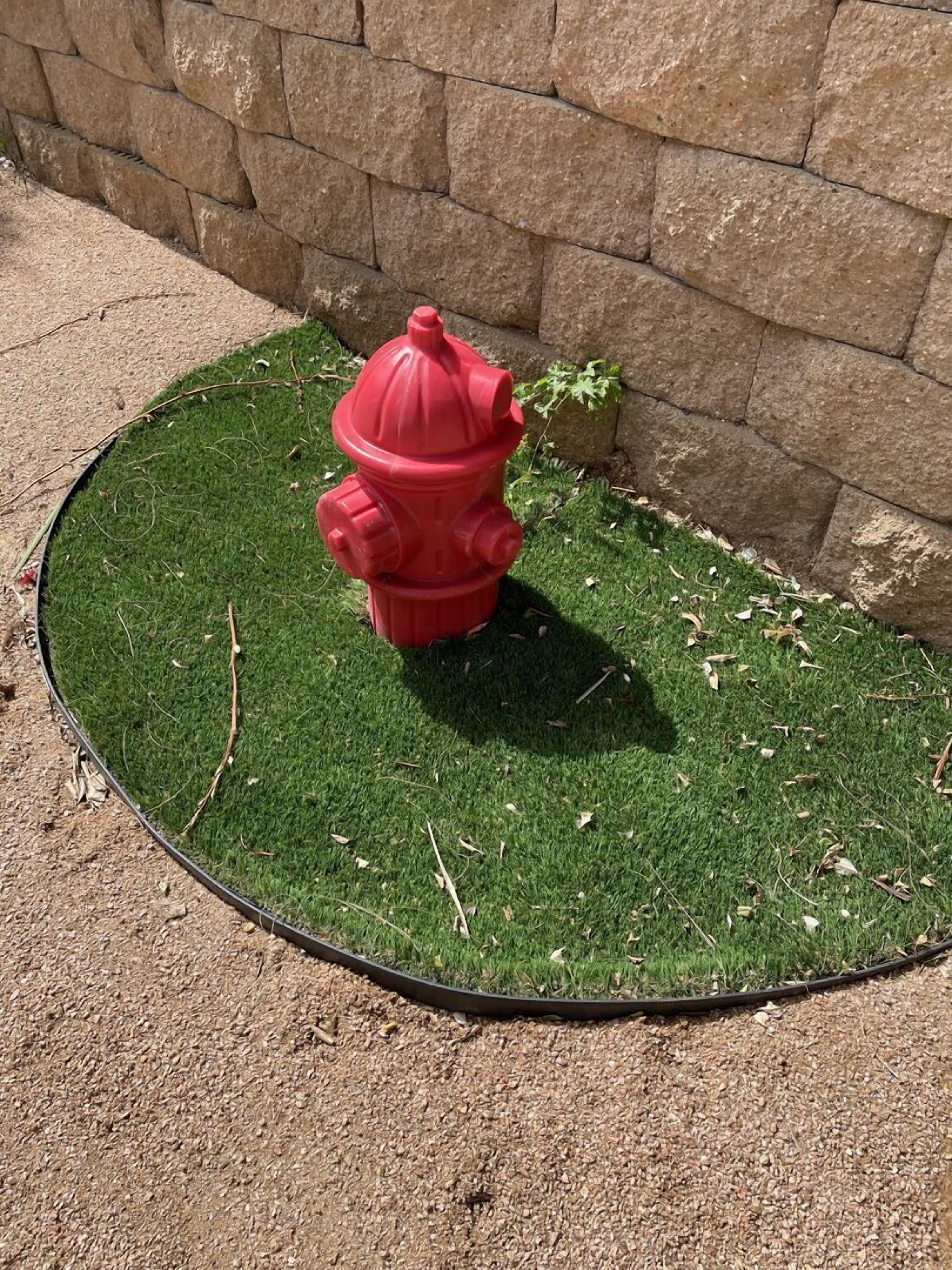 A red fire hydrant on artificial grass next to a stone wall.