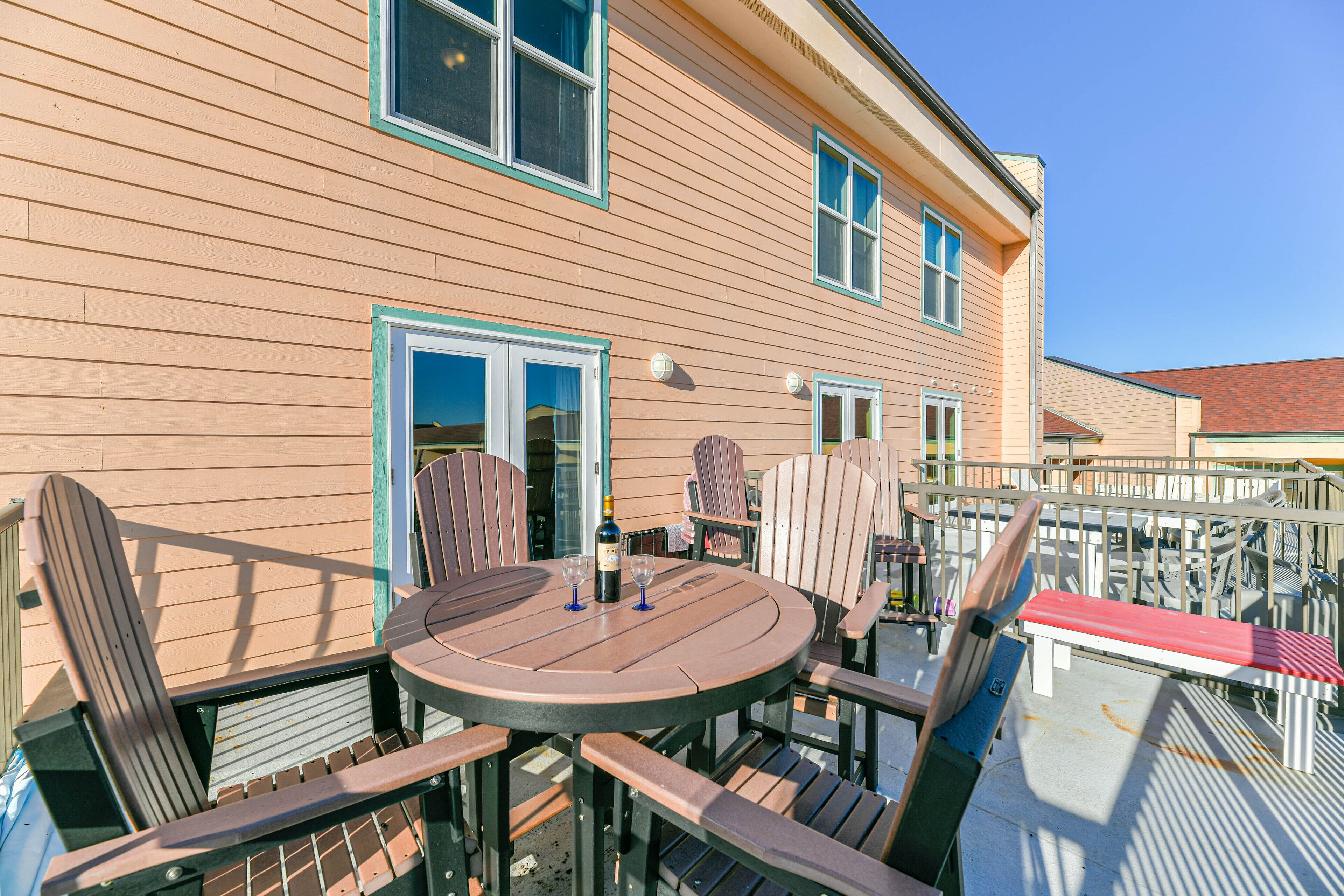 A wooden deck with Adirondack chairs and a round table, featuring a bottle and wine glasses.